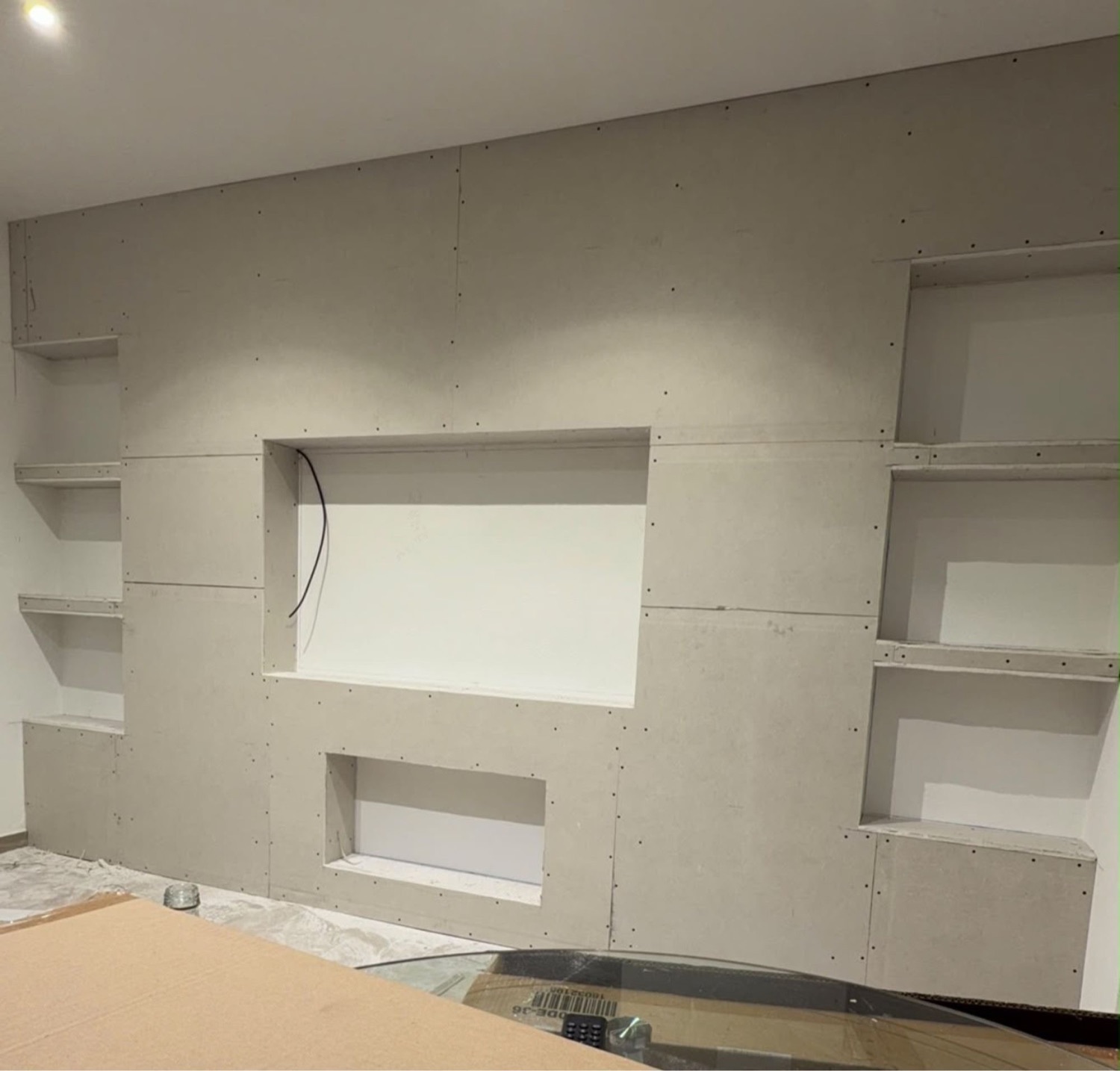 Parede de televisão em pladur com nichos e prateleiras laterais, em obra